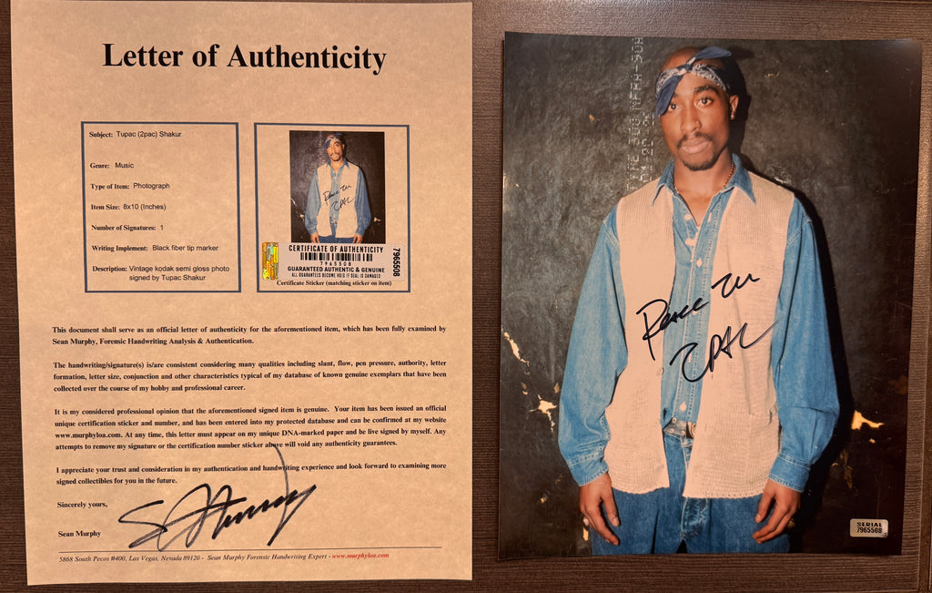 An autographed photo print of 2pac Tupac Shakur wearing a blue bandana, denim shirt, and beige vest, with a black signature across the center. The photo has a dark textured background and a small 'Authentic Signature' stamp in the lower right corner. signed autograph in black ink on a 8x12 inch photograph with COA.