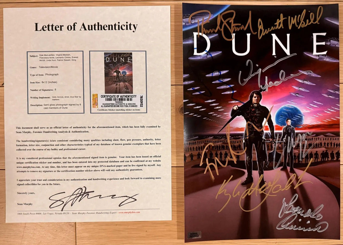 An autographed Dune movie poster featuring Paul Lauterbur, David McCallam, and Russell Crowe, signed in gold, silver, and blue ink, displayed on a light wood background with COA.