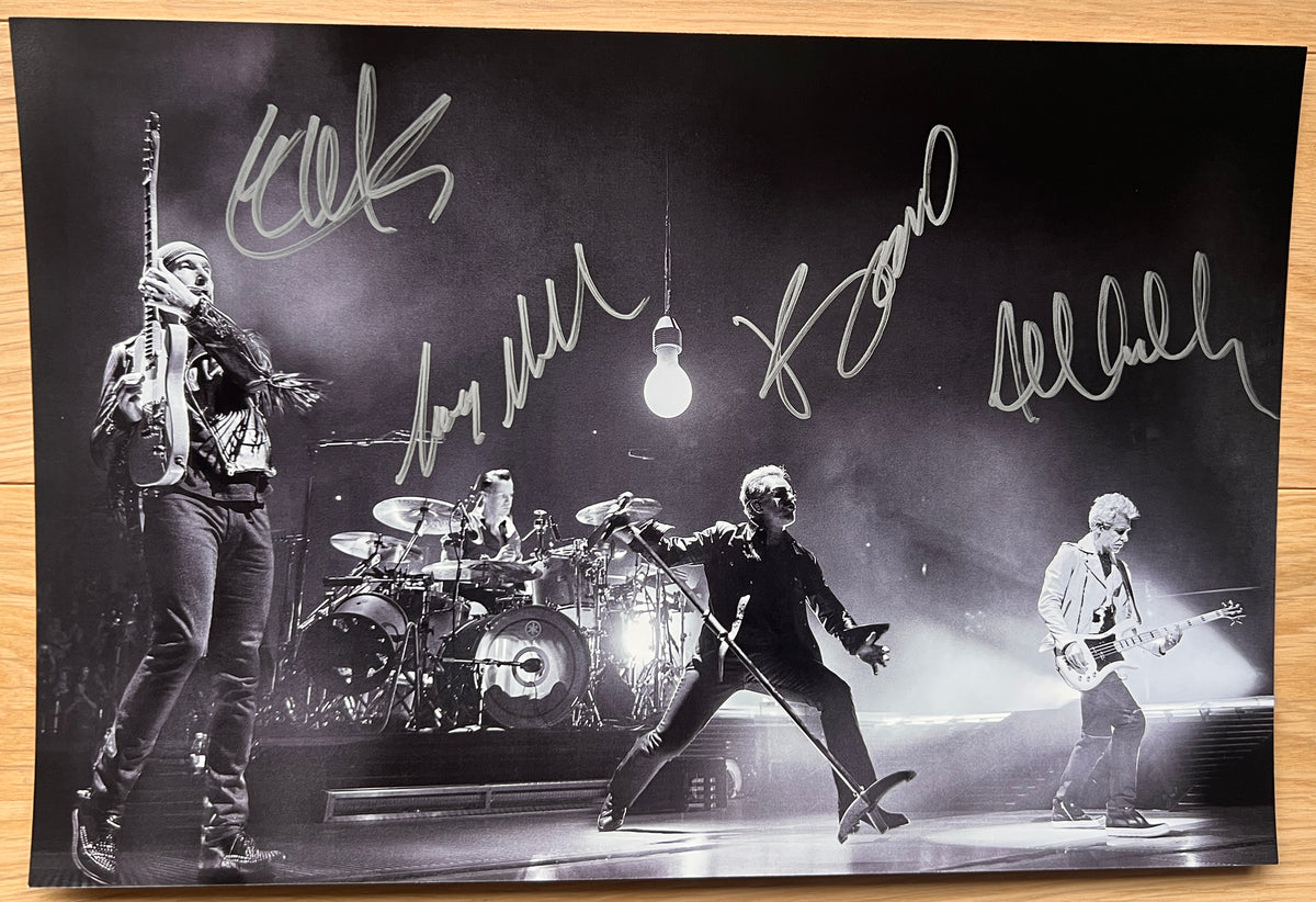 An autographed poster of the rock band U2. Signed photo of Bono, The Edge, Adam Clayton and Larry Mullen Jr in silver ink marker signatures. Photograph autographs for sale on 8x12 inch picture.