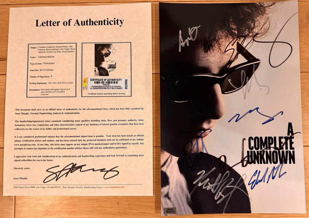 An autographed 8x12 photo print of the movie 'A Complete Unknown' featuring a close-up of a person wearing sunglasses, signed in blue, black, and silver marker with COA.