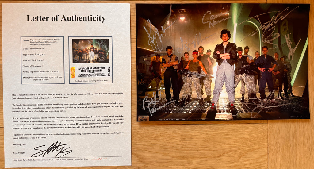 A signed collectible 8x12 photo print of the cast of the movie 'Alien' featuring autographs by multiple actors, displayed on a wooden surface with COA.