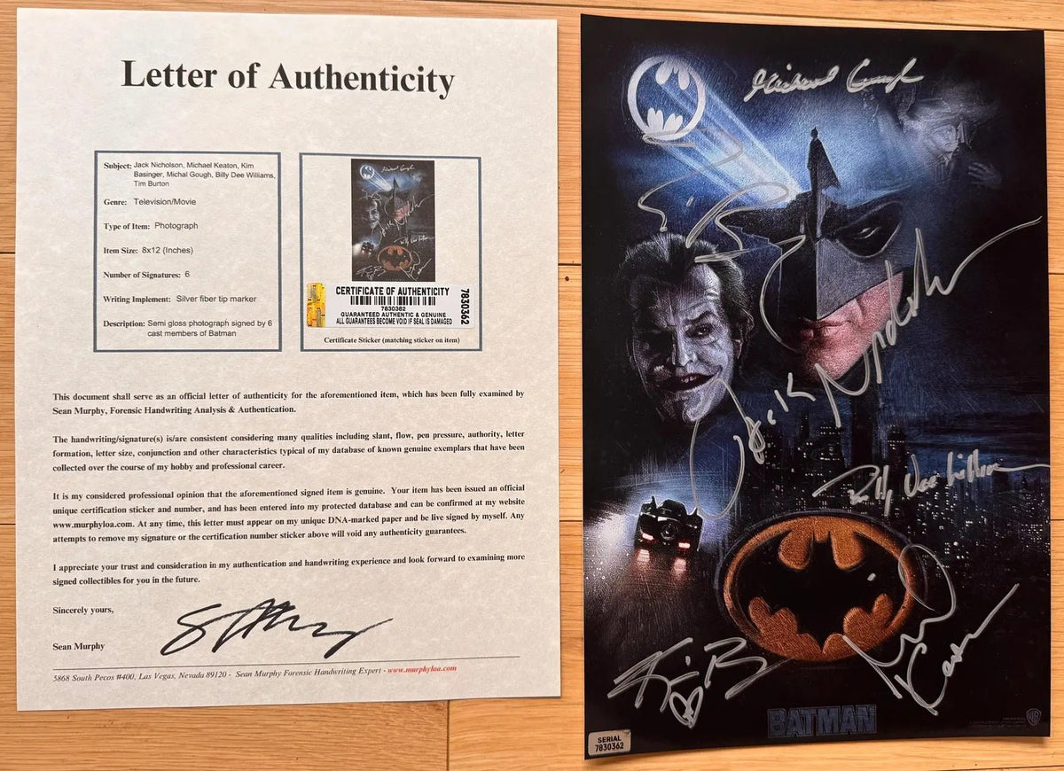 A signed 8x12 Batman photo featuring Michael Caine as the Joker, Michael Keaton as Batman, and signatures from multiple actors, displayed on a wooden surface with COA.