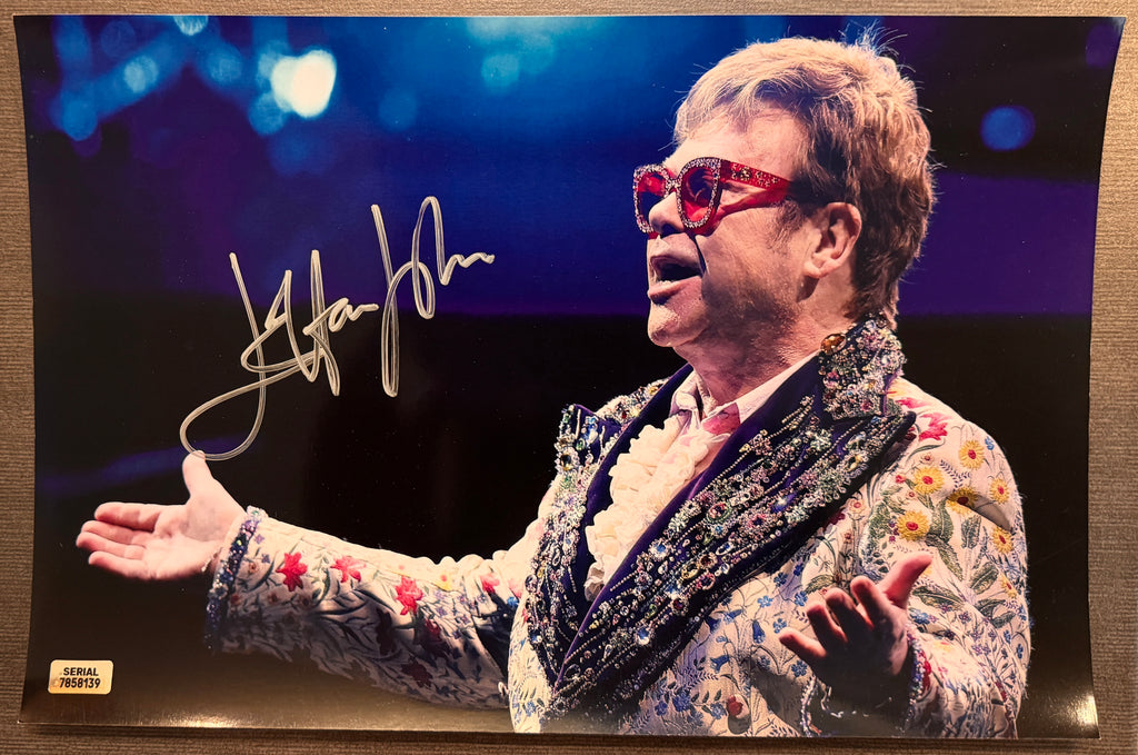 An autographed photo poster of the pop rock star musician, Elton John. Signed photograph in silver ink marker signatures. Photograph Elton John autographs for sale on 8x12 inch picture.