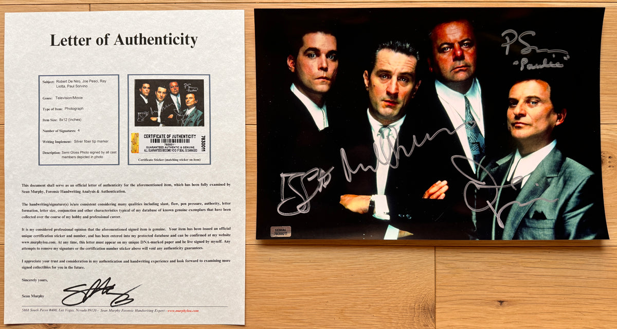 An autographed 8x12 photo print of the movie Goodfellas featuring the four main characters, signed in silver marker by Ray Liotta, Robert De Niro, Joe Pesci, and Paul Sorvino, displayed on a light wood background with COA.