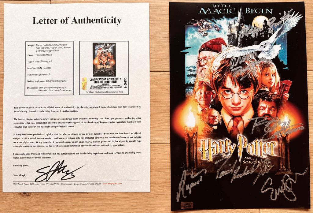 An autographed Harry Potter and the Sorcerer's Stone poster, signed by cast members including Daniel Radcliffe, Rupert Grint, and Emma Watson, displayed flat on a light wood surface with COA.