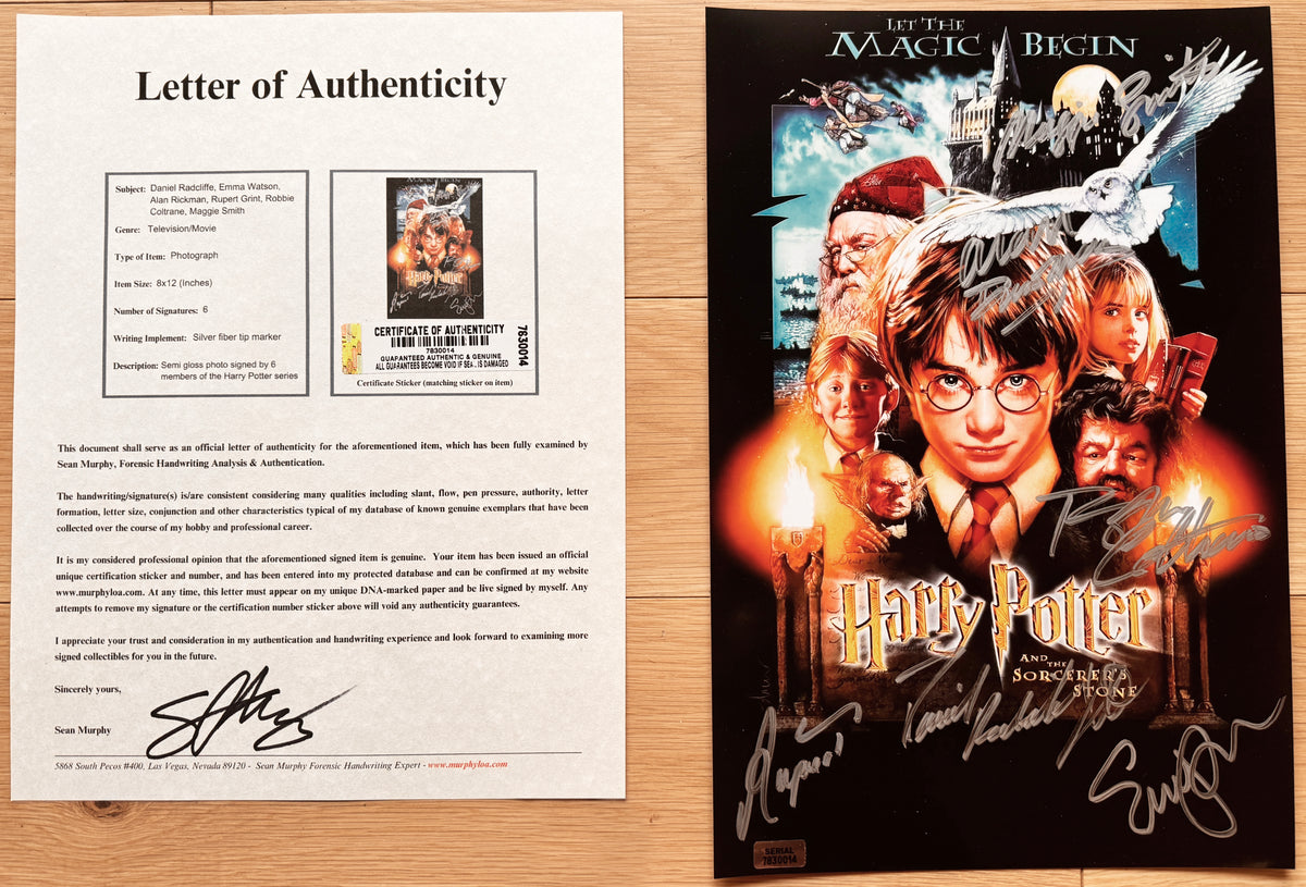 An autographed Harry Potter and the Sorcerer's Stone poster, signed by cast members including Daniel Radcliffe, Rupert Grint, and Emma Watson, displayed flat on a light wood surface with COA.
