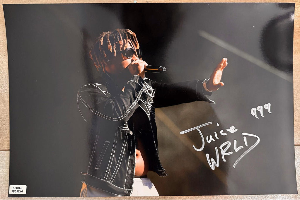 An autographed 8x10 photograph of rapper Juice WRLD performing on stage, signed in silver marker with the number 999. The photo shows him wearing sunglasses and a black jacket, with a small authentication label in the bottom-left corner. Photograph autographs for sale on 8x12 inch picture.