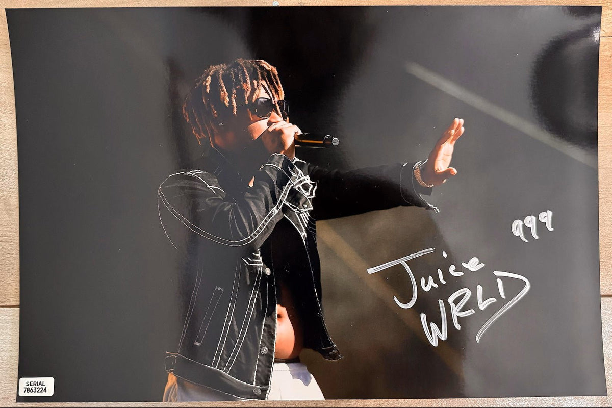 An autographed 8x10 photograph of rapper Juice WRLD performing on stage, signed in silver marker with the number 999. The photo shows him wearing sunglasses and a black jacket, with a small authentication label in the bottom-left corner. Photograph autographs for sale on 8x12 inch picture.