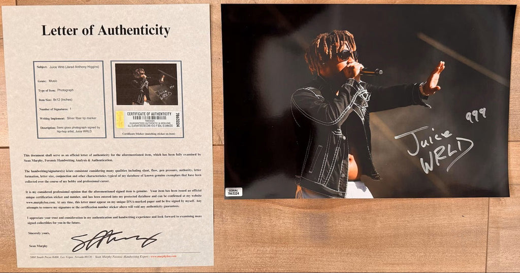 An autographed 8x10 photograph of rapper Juice WRLD performing on stage, signed in silver marker with the number 999. The photo shows him wearing sunglasses and a black jacket, with a small authentication label in the bottom-left corner with COA.