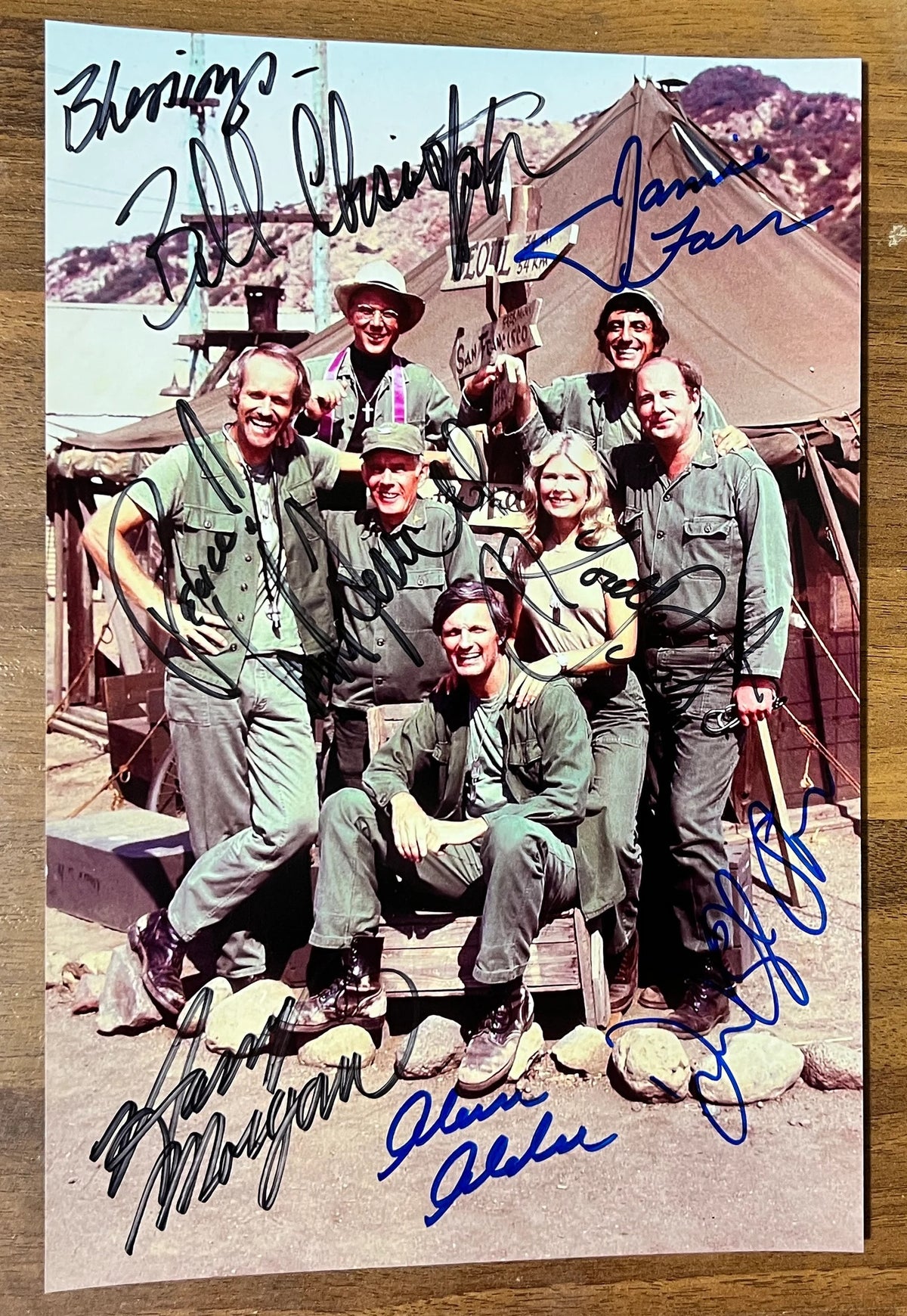 A cast autographed poster of the television series, MASH also known as M*A*S*H*. Signed photo of Alan Alda, Jamie Farr, Loretta Swit, William Christopher, Harry Morgan, Mike Farrell and David Ogden Stiers in blue and black ink marker signatures. Photograph autographs for sale on 8x12 inch picture.