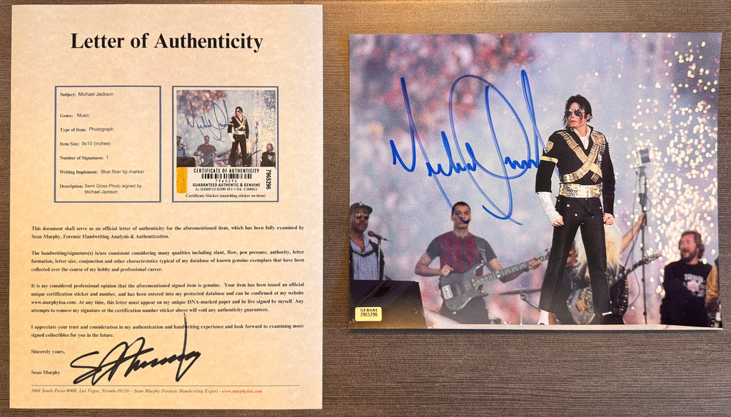 An autographed 8x10 photograph of Michael Jackson performing on stage, signed in blue ink across the center. The photo shows Michael Jackson in a black and gold with COA