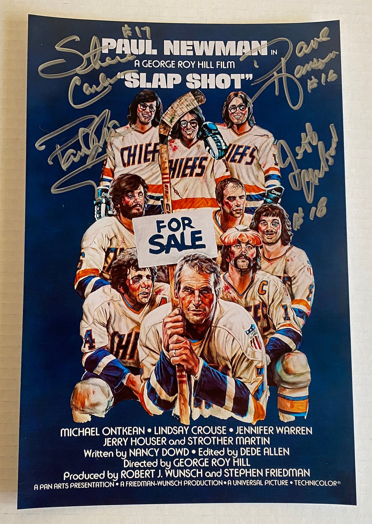 A cast autographed poster of the hockey movie, Slap Shot also known as Slapshot. Signed photo of Paul Newman, Jeff Carlson, Steve Carlson and Dave Hanson in silver ink marker signatures. Photograph Slap Shot autographs for sale on 8x12 inch picture.