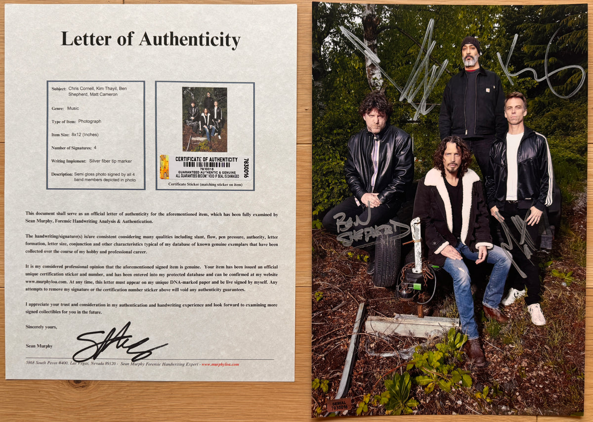 A signed photo print of the band Soundgarden, featuring the four members posing outdoors in a wooded setting, with silver autographs written across the top and bottom with COA.
