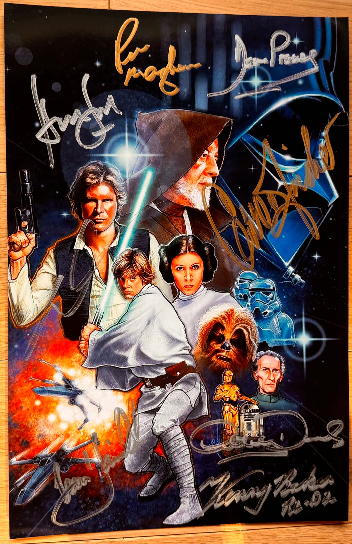 A cast autographed Star Wars movie poster. Signed photo of Harrison Ford, Carrie Fisher, Mark Hamill, Peter Mayhew, George Lucas, Anthony Daniels, David Prowse and Kenny Baker in gold and silver ink marker signatures. Photograph autographs for sale on 8x12 inch picture.