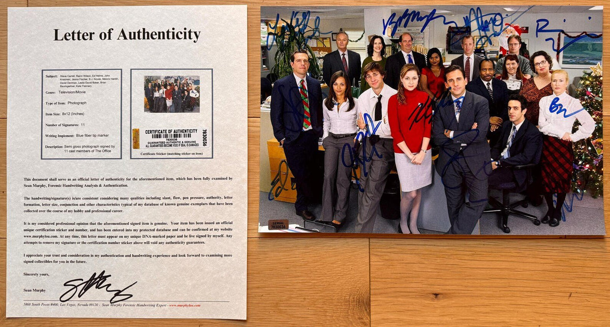 An autographed photo print of the cast of the TV show 'The Office' posed in their office, signed in blue ink by Steve Carell, John Krasinski, Fenna Fischer, Rainn Wilson and more across the group, autograph in blue ink on 8x12 inch photograph with COA.