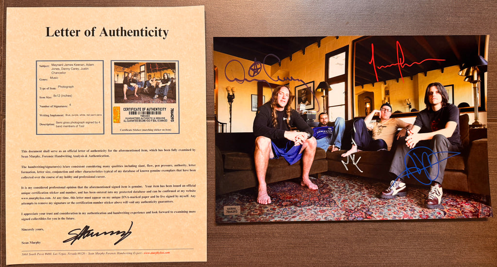 An autographed 8x12 photo print of the band Tool, featuring the four members sitting in a living room. The photo is signed in red, blue, and white marker with COA.