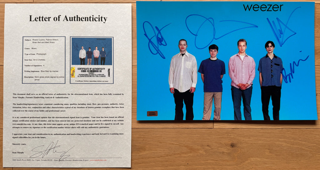 A signed 8x12 Weezer photo featuring the band members standing in front of a bright blue background with COA.