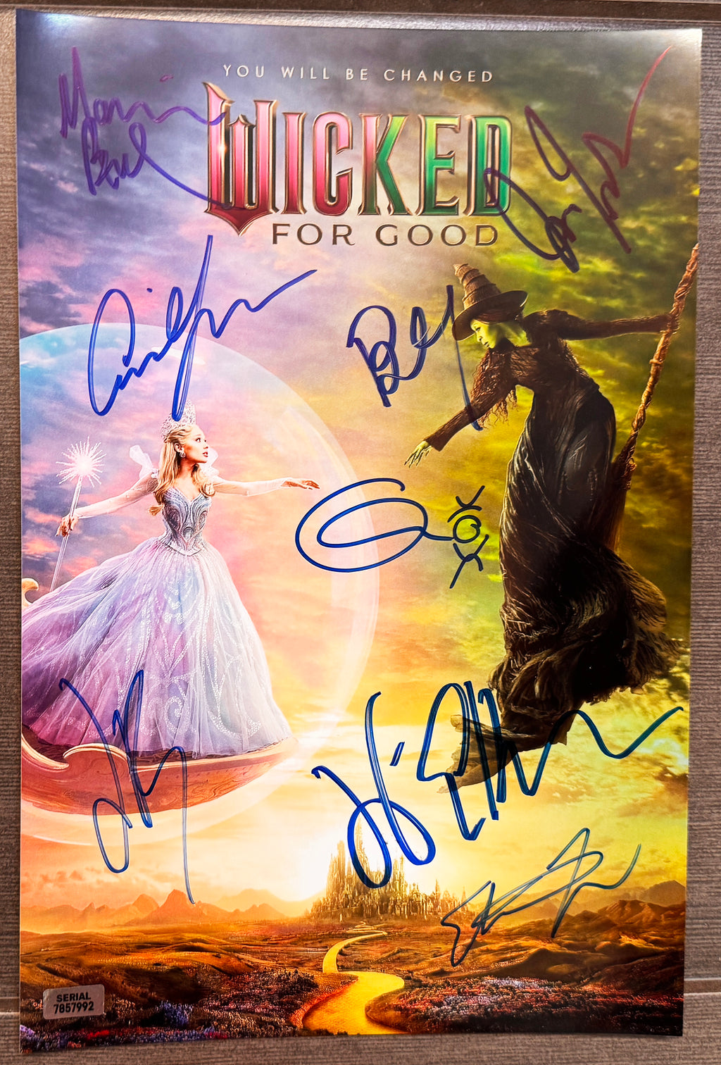 A signed and autographed 'Wicked for Good' poster featuring the Wizard of Oz and the Wicked Witch of the West, signed in blue ink autographs by Ariana Grande, Cynthia Erivo, Jonathan Bailey, Marissa Bode, Ethan Slater, Bowen Yang, Jeff Goldblum and Michelle Yeoh. autograph on 8x12 inch photograph photo autographs for sale.