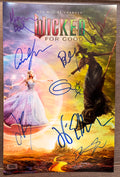 A signed and autographed 'Wicked for Good' poster featuring the Wizard of Oz and the Wicked Witch of the West, signed in blue ink autographs by Ariana Grande, Cynthia Erivo, Jonathan Bailey, Marissa Bode, Ethan Slater, Bowen Yang, Jeff Goldblum and Michelle Yeoh. autograph on 8x12 inch photograph photo autographs for sale.